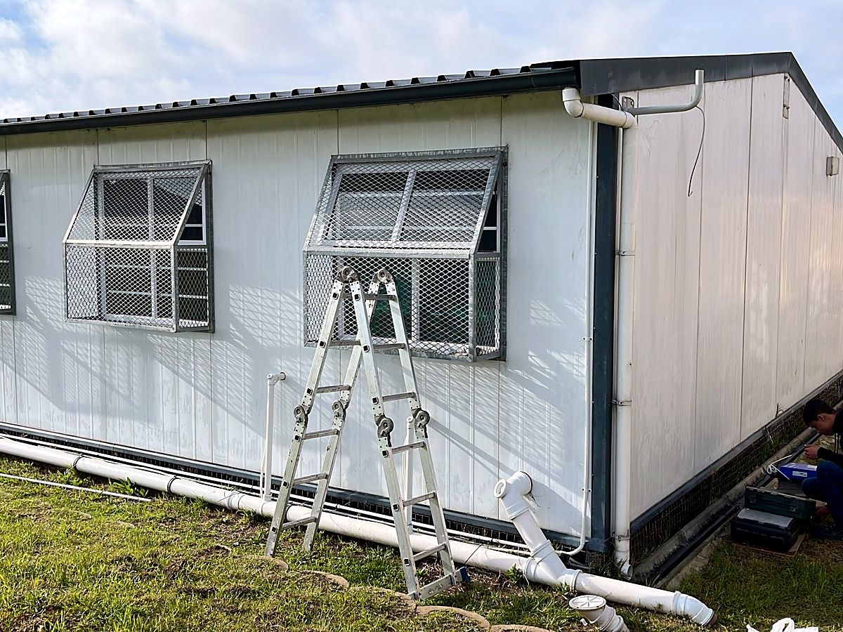 Technician running network cable in conduit beside prefab school classrooms